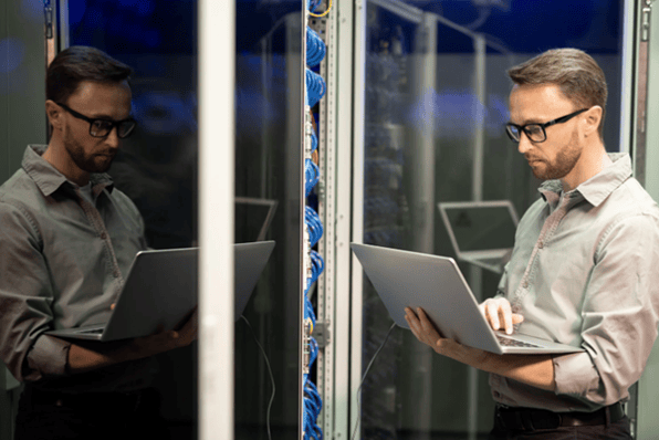 IT professional working on a laptop in a server room representing IT support managed services and business infrastructure management.