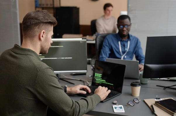 IT professionals performing system security checks and coding on laptops in an office environment representing cybersecurity and penetration testing services. 